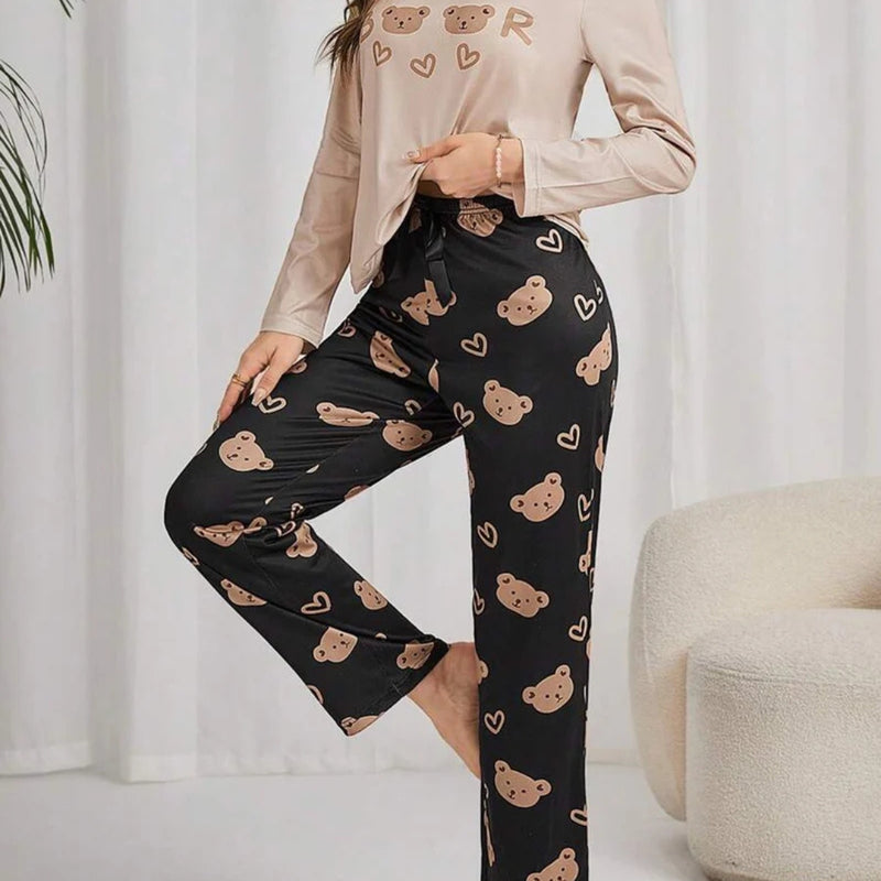 Mulher usando pijama longo feminino com blusa bege e calça preta estampada com rostos de ursinhos e corações, ideal para conforto e estilo em noites amenas.