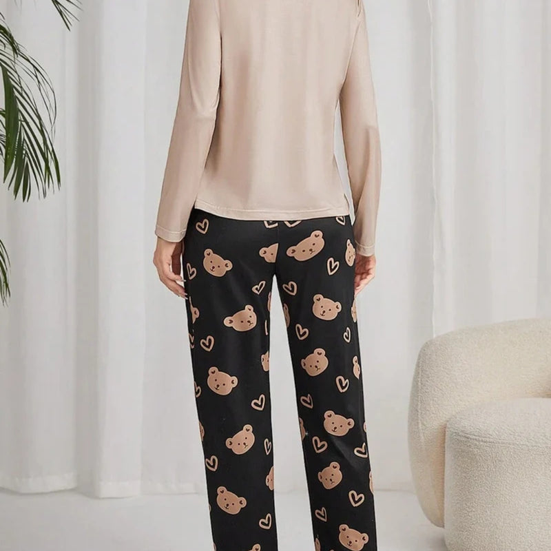 Mulher usando pijama longo feminino com blusa bege e calça preta estampada com rostos de ursinhos e corações, ideal para conforto e estilo em noites amenas.
