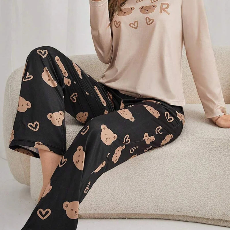 Mulher usando pijama longo feminino com blusa bege e calça preta estampada com rostos de ursinhos e corações, ideal para conforto e estilo em noites amenas.