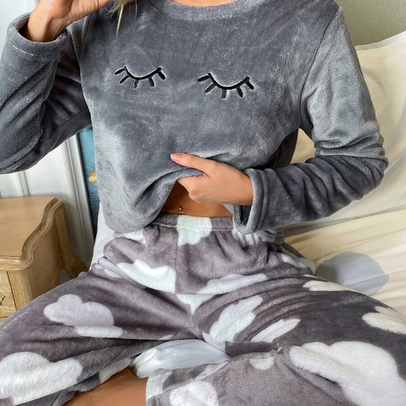 Mulher vestindo o Pijama Longo Cílios em tecido peluciado com estampa de nuvem e bordado de cílios nos olhos, ideal para noites frias e cheias de conforto.

