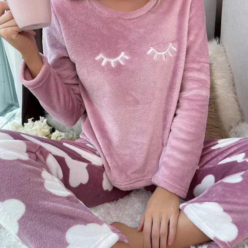 Mulher vestindo o Pijama Longo Cílios em tecido peluciado com estampa de nuvem e bordado de cílios nos olhos, ideal para noites frias e cheias de conforto.

