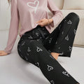 Pijama longo feminino com blusa rosa claro e estampa de coração branco. Acompanha calça preta com desenhos de coração e ajuste em laço. Conforto com romantismo.

