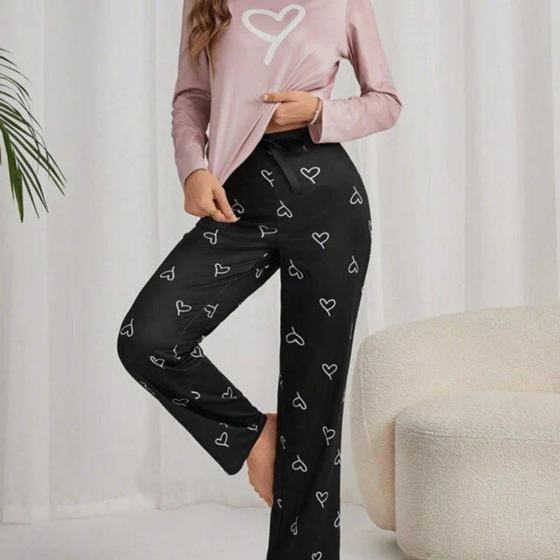 Pijama longo feminino com blusa rosa claro e estampa de coração branco. Acompanha calça preta com desenhos de coração e ajuste em laço. Conforto com romantismo.

